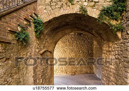 Stock Photo - View of medieval stone arch in village, part of external tower gate of town walls, showing entrance to tower both through arch and steps ascending, seen from within the village.. Fotosearch