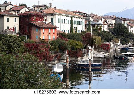 Stock Image - View of Ossuccio village houses seen from shoreline of Lake Como, with boats moored, and ivy turning red in autumn pale afternoon sunlight, Northern Italy. Fotosearch