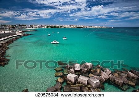 View of Otranto harbour with clear green water, moored sailboats and motorboats, medieval fortifications and town beyond, sunny spring morning with dramatic clouds in blue sky, Salento, Puglia, Southern Italy View Large Photo Image Picture - View of Otranto harbour with clear green water, moored sailboats and motorboats, medieval fortifications and town beyond, sunny spring morning with dramatic clouds in blue sky, Salento, Puglia, Southern Italy. Fotosearch