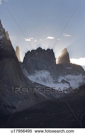 Stock Photography - View of snow covered Los Torres, Torres del Paine backlit in late afternoon autumn sunshine with god beams, Southern Cile, Patagonia. Fotosearch