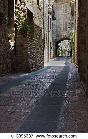 Stock Photo - View of stone paved street with medieval stone buildings lining each side, and connecting arch above, on sunny afternoon, Assisi, Umbria, Italy. Fotosearch