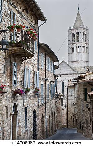 Stock Photo - View of stone paved street with medieval stone buildings, and decorative plants lining each side, campanile tower and church of Santa Chiara church beyond, on sunny afternoon, Assisi, Umbria, Italy. Fotosearch