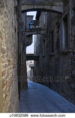 Stock Photograph - View of stone paved street with medieval stone buildings lining each side, and connecting arches above, Montefalco, Umbria, Italy. Fotosearch