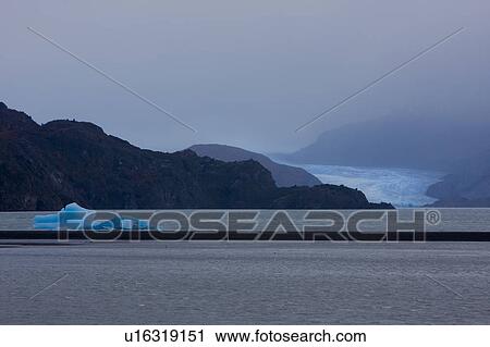 Stock Image - View of stormy grey Lago Grey with bright blue iceberg fragment floating in front of glacier, and snow covered mountains in background, Torres del Paine, Southern Chile, Patagonia. Fotosearch