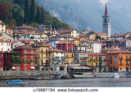 Picture - View over lake of town of Varenna along lake shore with mountain range beyond on calm autumn afternoon in pale sunlight, Lake Como, Northern Italy. Fotosearch