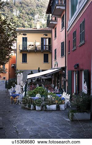 Village street view with single man sitting reading in outdoor cafe, paved stone street, stucco facades of houses painted red, orange, yellow, with green window shutters, typical of Northern Italy View Large Photo Image Stock Image - Village street view with single man sitting reading in outdoor cafe, paved stone street, stucco facades of houses painted red, orange, yellow, with green window shutters, typical of Northern Italy. Fotosearch