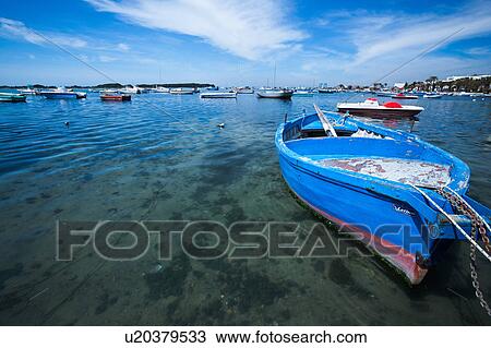 Stock Image - Wooden painted blue fishing boat moored in Porto Cesareo harbour, with rest of harbour in background, sunny spring morning, Salento, Puglia, Southern Italy. Fotosearch