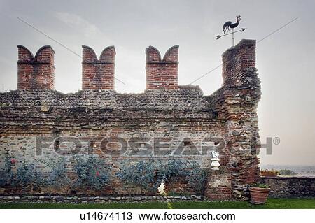Stock Image - Large brick wall with rooster weathervane. Fotosearch