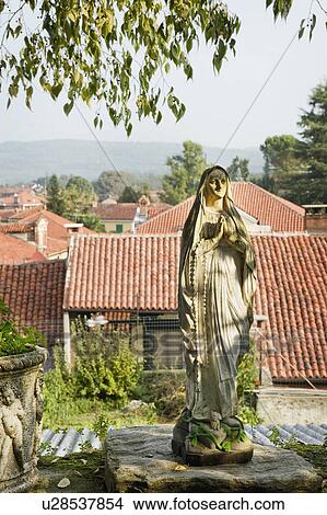 Stone virgin Mary statue against red tile roofs View Large Photo Image Picture - Stone virgin Mary statue against red tile roofs. Fotosearch