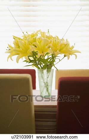 Stock Image - Vase of yellow flowers on red and gold kitchen table. Fotosearch