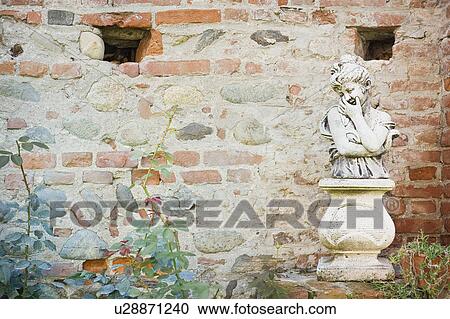 Stock Image - Young girl statue along brick wall. Fotosearch