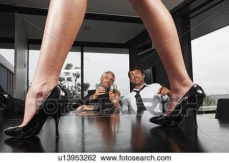 Stock Image - Businessmen, looking up at a woman standing on a table.. Fotosearch