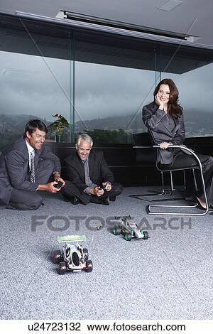Stock Image - Businessmen playing with toy automobiles. Fotosearch