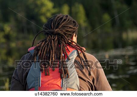 Stock Image - Back view of a man with dreadlocks wearing a life jacket at Lake of the Woods, Ontario. Fotosearch