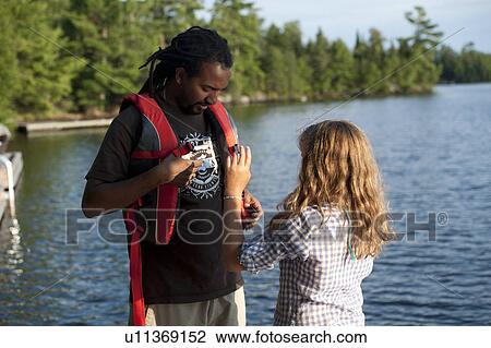 Blond girl helping Africian American man with his life jacket at Lake of the Woods, Ontario View Large Photo Image Stock Image - Blond girl helping Africian American man with his life jacket at Lake of the Woods, Ontario. Fotosearch
