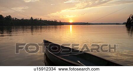 Picture - Bow of a canoe with the sunset in the horizon at Lake of the Woods, Ontario. Fotosearch