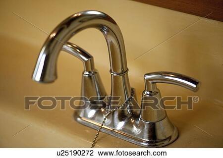 Stock Image - Chrome bathroom double handle faucet and taps with a plug chain on a yellow basin. Fotosearch