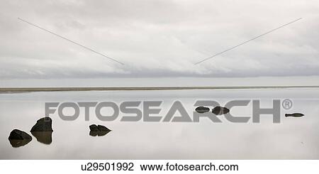 Cloudy sky, reflected in calm water, with rocks breaking the ocean surface View Large Photo Image Stock Image - Cloudy sky, reflected in calm water, with rocks breaking the ocean surface. Fotosearch
