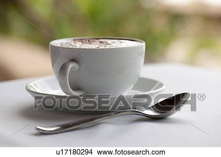 Cofffee cup, saucer and teaspoon, filled with steamed milk and sprinkled with spice, on a white table View Large Photo Image Picture - Cofffee cup, saucer and teaspoon, filled with steamed milk and sprinkled with spice, on a white table. Fotosearch