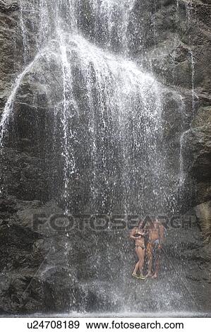 Stock Photo - Couple standing under a waterfall cascading over steep rock face. Fotosearch