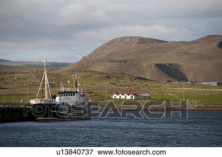 Stock Photo - Fishing trawler moored in harbour with hilly rural farm landscape. Fotosearch