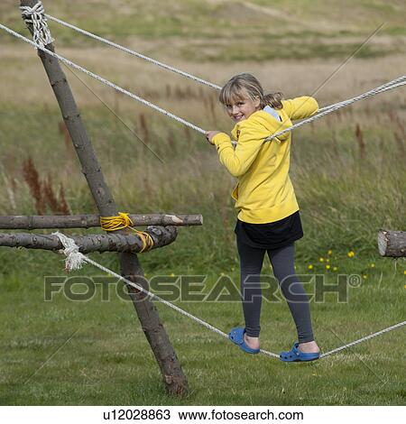 Stock Image - Girl balancing on rope bridge structure. Fotosearch