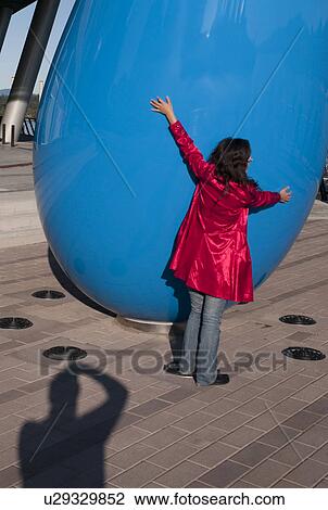 Stock Image - Girl in a red coat hugging a large sculpture in Vancouver, British Columbia, Canada. Fotosearch