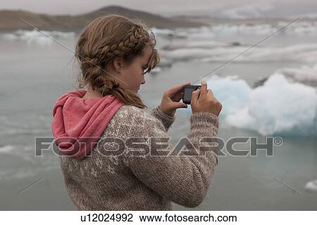 Girl photographer in an Icelandic sweater and a coral hoodie focussing on blue icebergs in a glacial lake View Large Photo Image Stock Image - Girl photographer in an Icelandic sweater and a coral hoodie focussing on blue icebergs in a glacial lake. Fotosearch