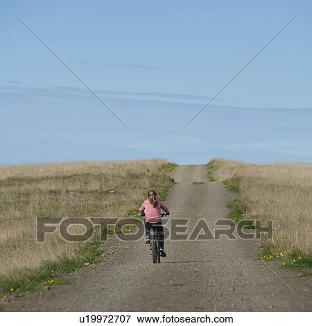 Stock Photo - Girl riding bicycle on empty rural road. Fotosearch