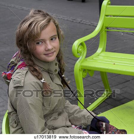 Stock Photo - Girl sitting on park bench on sidewalk. Fotosearch