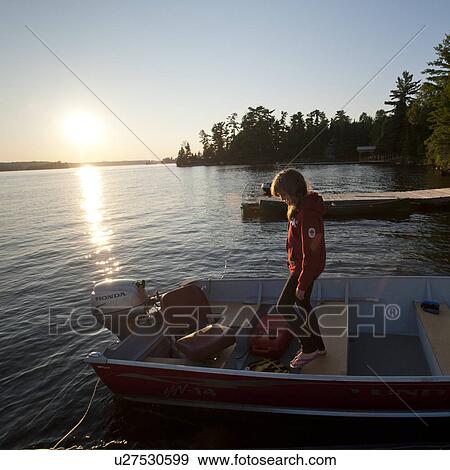 Stock Photo - Girl standing in a motorboat with horizon sunset at Lake of the Woods, Ontario. Fotosearch