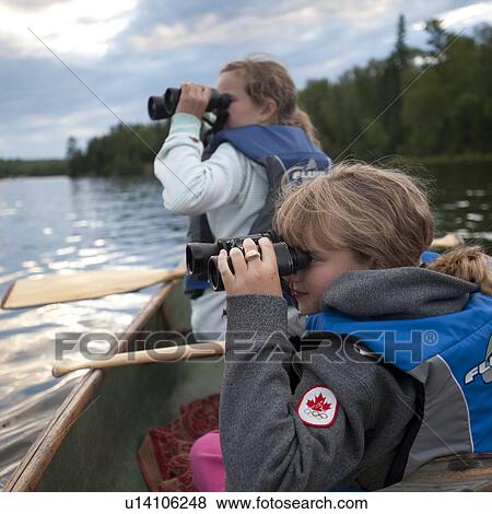 Stock Photo - Girls in a row boat looking through binoculars at Lake of the Woods, Ontario. Fotosearch
