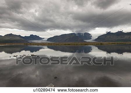 Grey mountains glaciers and dark clouds reflected in the lake View Large Photo Image Picture - Grey mountains glaciers and dark clouds reflected in the lake. Fotosearch