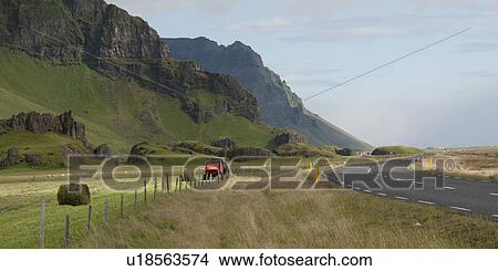 Hay baler making bales on farmland between mountainside and highway View Large Photo Image Picture - Hay baler making bales on farmland between mountainside and highway. Fotosearch