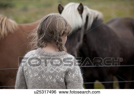 Stock Photograph - Head and back of girl with messy hair in knit sweater in front of Icelandic horses. Fotosearch