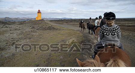 Stock Photo - Horse ride on a path towards a lighthouse. Fotosearch