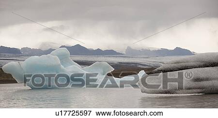 Stock Photo - Icebergs floating in the ocean along a misty mountainous coastline. Fotosearch