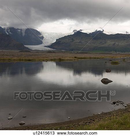 Stock Image - Landscape, glacier through mountain valley, reflected in glacial lake. Fotosearch