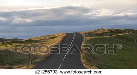 Stock Image - Landscape, highway disappearing over the horizon through farmland, on a cloudy day. Fotosearch