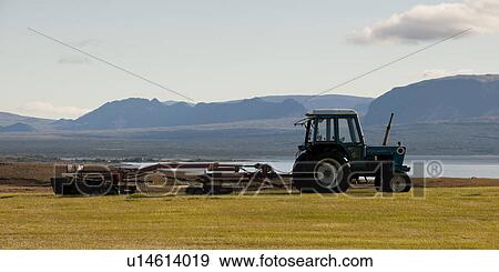 Stock Photo - Landscape, tractor pulling farm machinery before rugged mountain. Fotosearch
