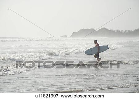 Stock Photo - Male surfer on an overcast day on the beach. Fotosearch