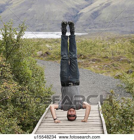 Picture - Man doing headstand on boardwalk in hilly countryside. Fotosearch