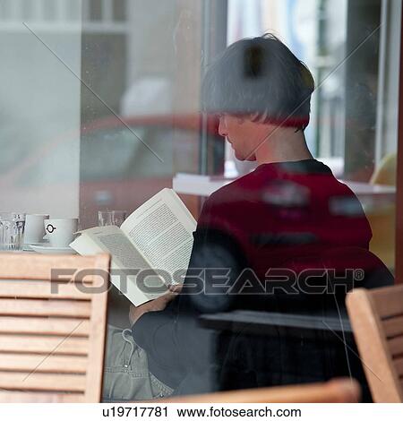 Stock Image - Man in a cafe reading a book, through a window. Fotosearch