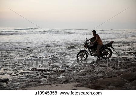 Stock Photo - Man on a motorcycle in a cool evening sunset over the calm beach Costa Rica . Fotosearch