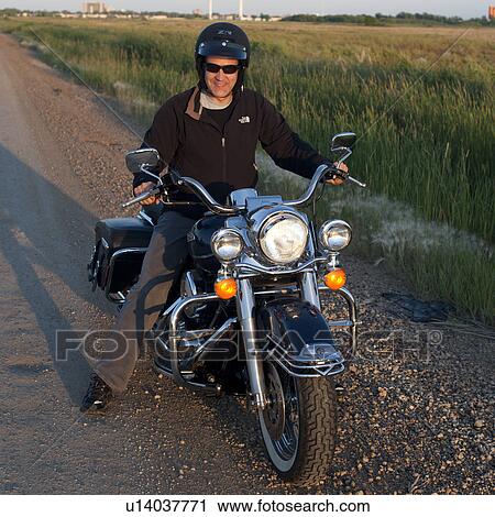 Stock Image - Man on a motorcycle on roadway at Lake of the Woods, Ontario. Fotosearch
