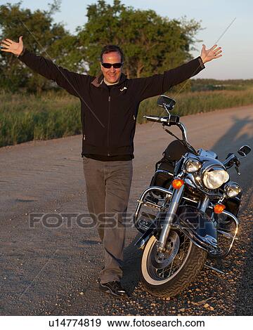 Stock Photo - Man standing beside a motorcycle in Lake of the Woods, Ontario. Fotosearch