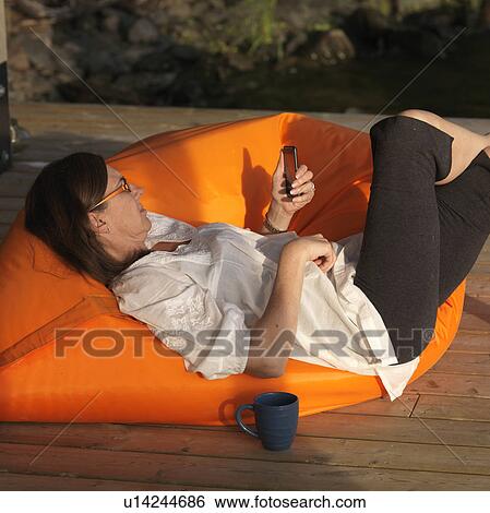 Mature woman lounging in a chair looking at her cell phone at Lake of the Woods, Ontario View Large Photo Image Stock Photograph - Mature woman lounging in a chair looking at her cell phone at Lake of the Woods, Ontario. Fotosearch