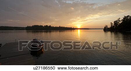 Stock Image - Motorboat at the dock with the sunsest in the horizon in Lake of the Woods, Ontario. Fotosearch