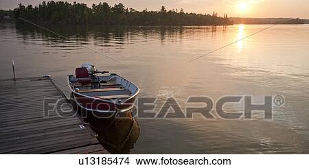 Picture - Motorboat at the edge of a dock with the horizon sunset at Lake of the Woods, Ontario. Fotosearch