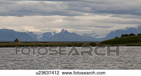 Stock Image - Mountains and glaciers of Iceland, with grassland, and a shed, from the coastline. Fotosearch